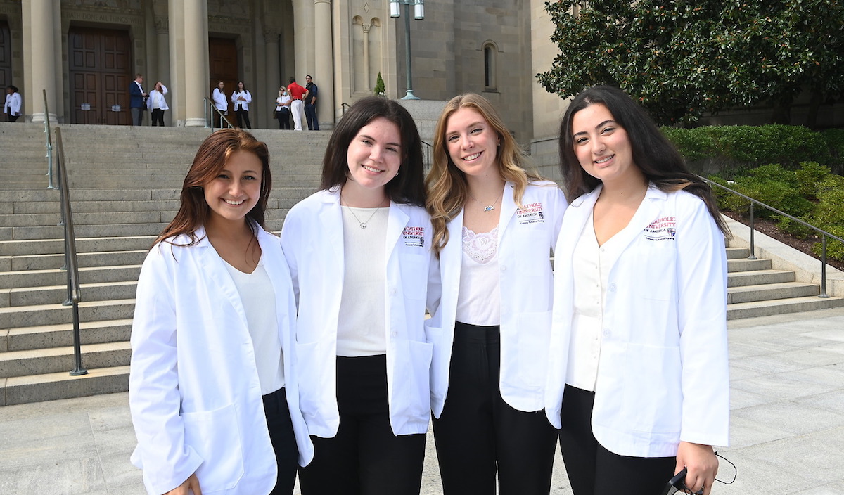 Four female nursing students in their white coats on the steps of the Basilica of the National Shrine of the Immaculate Conception