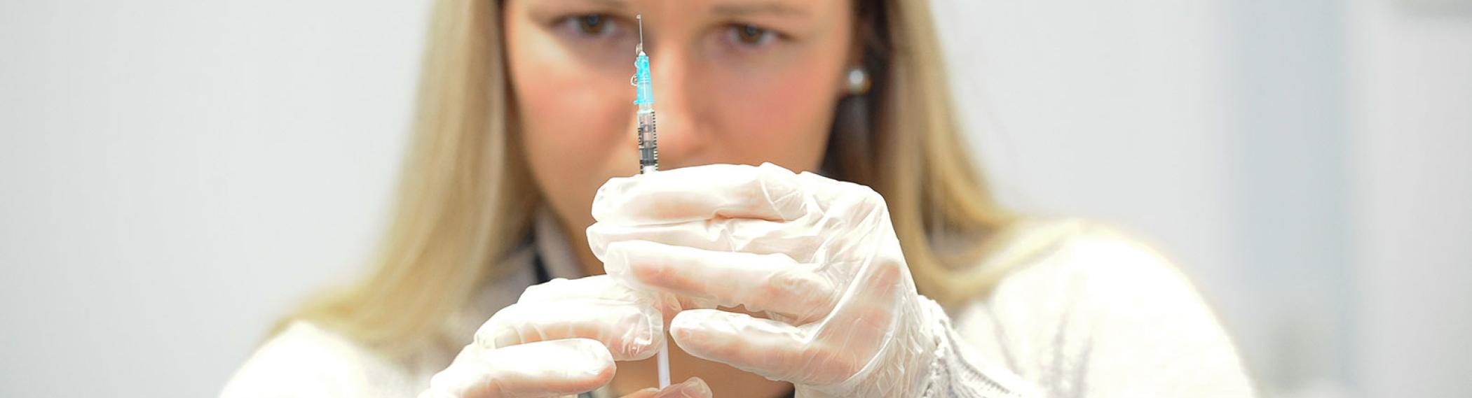Nursing researcher examining fluid in a syringe.