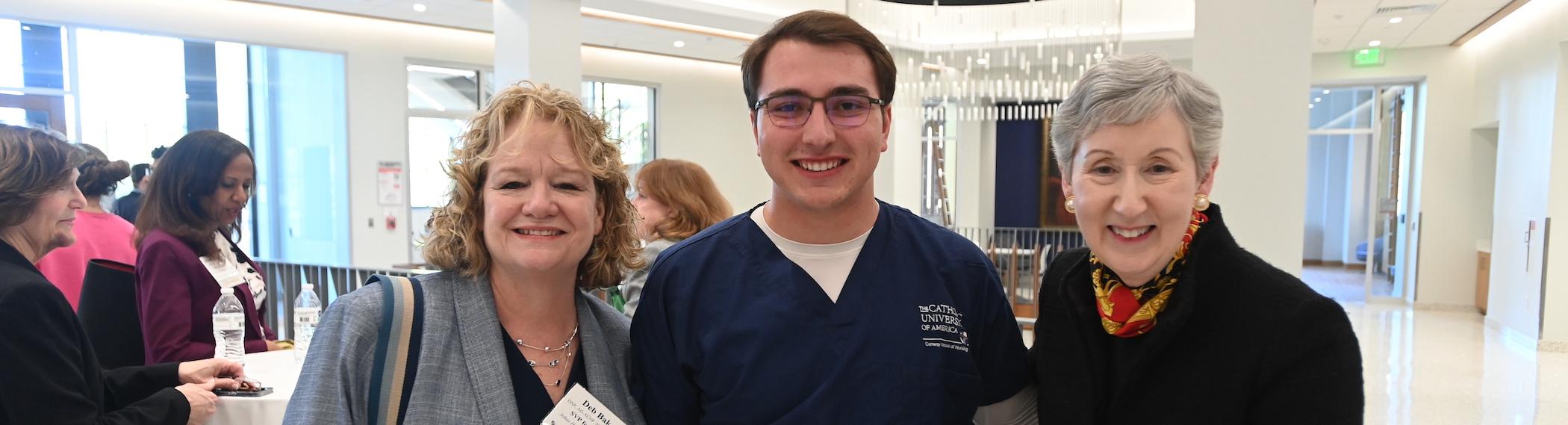 two alumni pose for a photo with nursing dean marie nolan