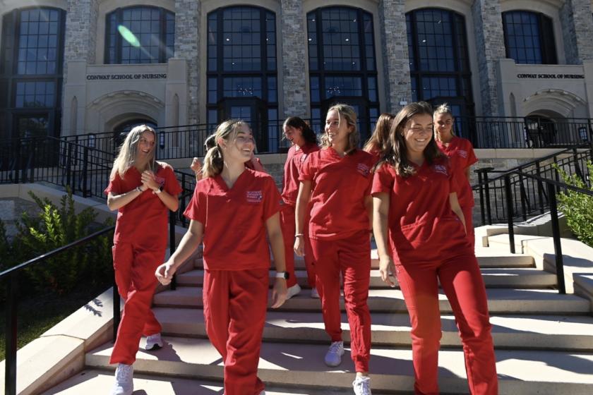 nursing students dressed in their red scrubs walking down the steps of the nursing building