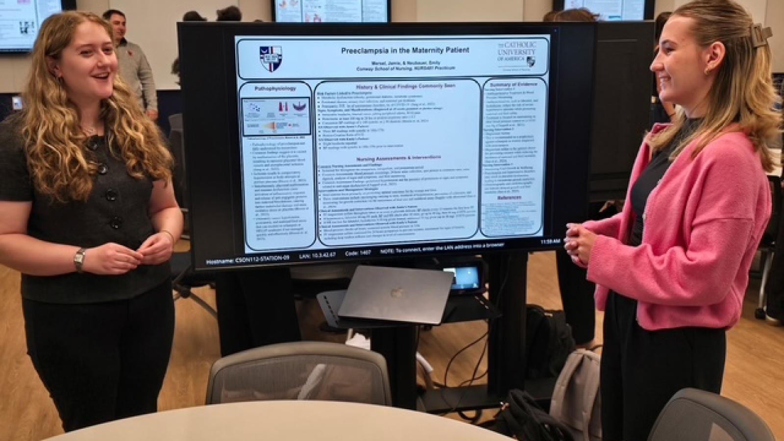 Presentation from 2026 Senior Practicum Presentations, featuring two female students discussing their project.