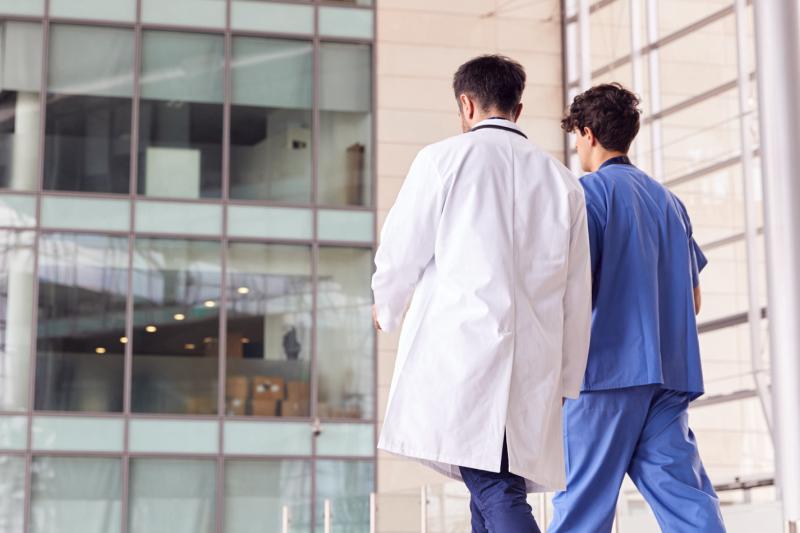 a male nurse and doctor, outside, walking away from the hospital
