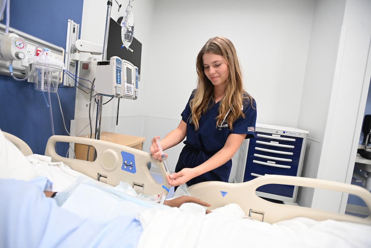 student filling an IV in a simulation hospital room at the nursing school