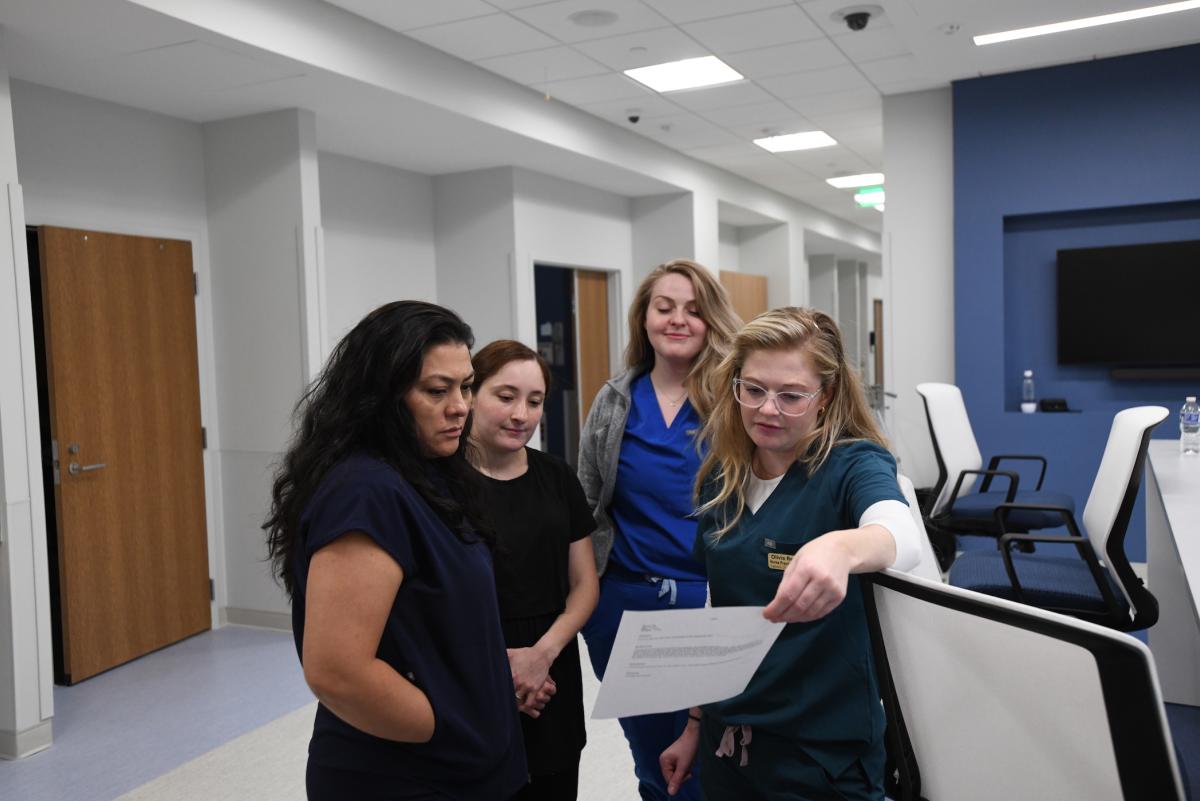 studdents and instructors reviewing a paper in the simulation area of the conway school of nursing