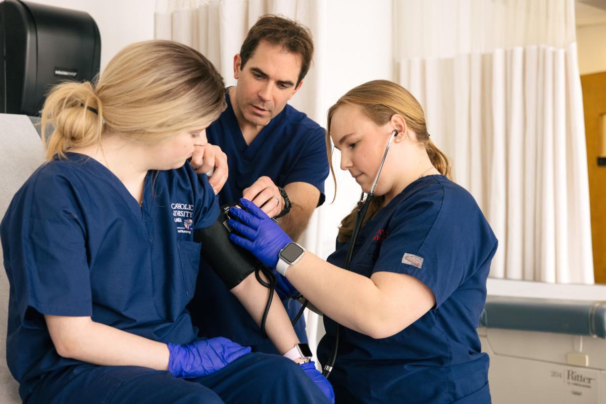 students and a professor checking someone's blood pressure in a nursing simulation