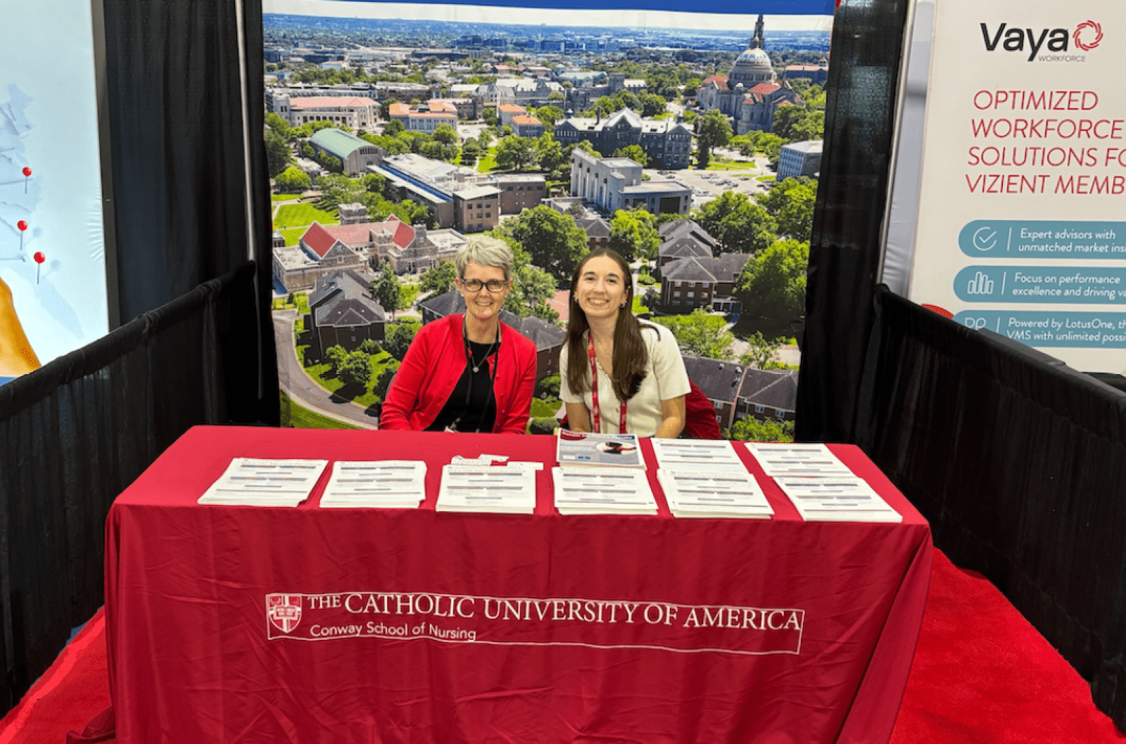 A Conway Nursing professor and student sitting behind a table at a conference.