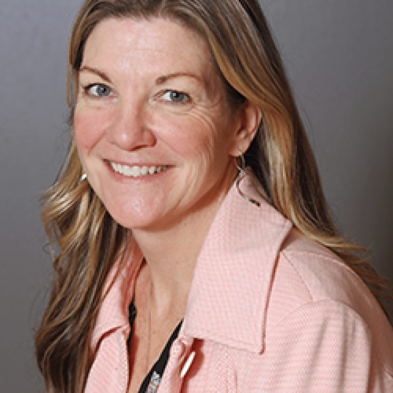 Photo of Cari Selzer. She has long blonde hair and is wearing a pink blazer.