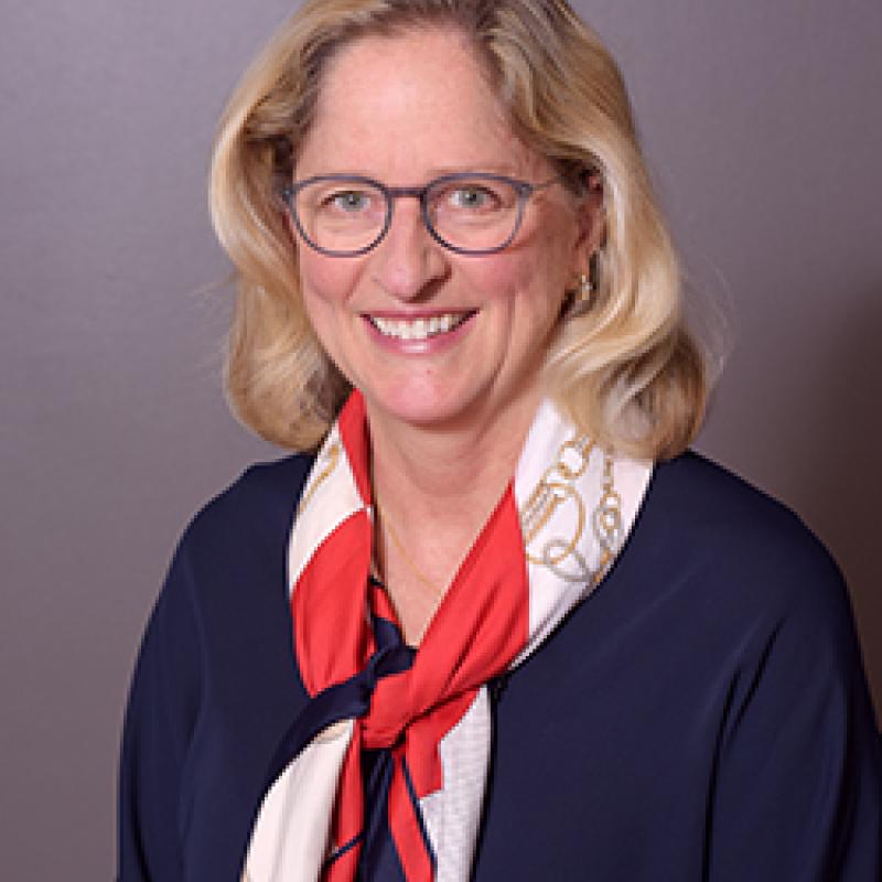 Photo of Jill Dombrowski. She has shoulder-length blonde hair and is wearing a blue and red scarf over a navy shirt.