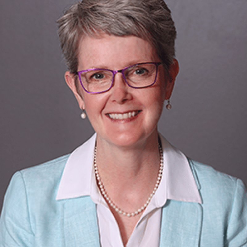 Photo of Martha Scheckel. She has short grey hair and is wearing a light blue blazer over a white shirt.