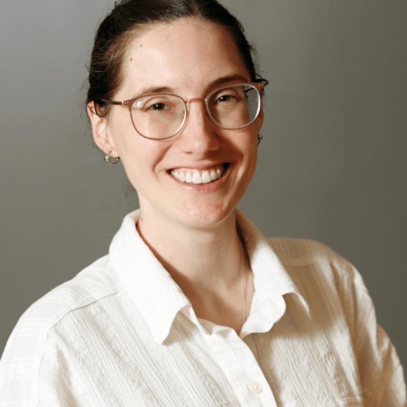 Photo of Kyra Mendez. She has her brown hair in a bun and is wearing brown glasses and a white shirt.