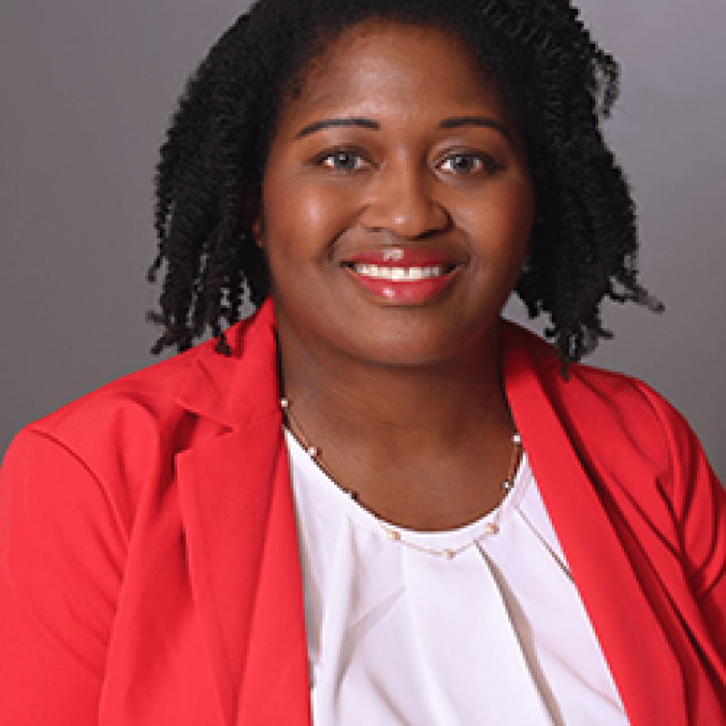 A photo of Shanna Fortune. She has curly black hair and is wearing a pink blazer over a white shirt.