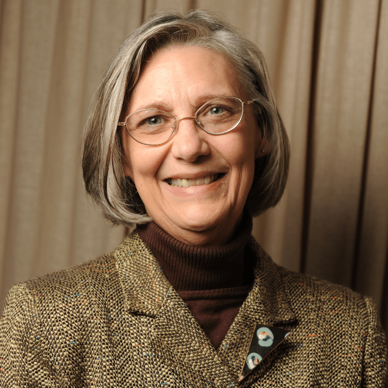 Photo of Mary A. Paterson. She has a grey bob and is wearing a tweed blazer over a brown turtleneck.