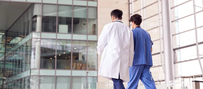 a male nurse and doctor, outside, walking away from the hospital