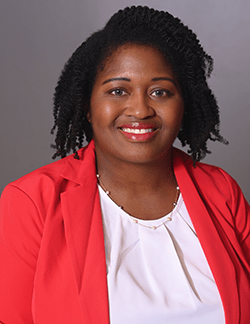 A photo of Shanna Fortune. She has curly black hair and is wearing a pink blazer over a white shirt.